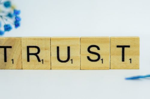 a wooden block that says trust, surrounded by blue flowers