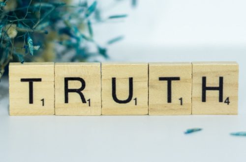 a wooden block spelling truth next to a bouquet of flowers